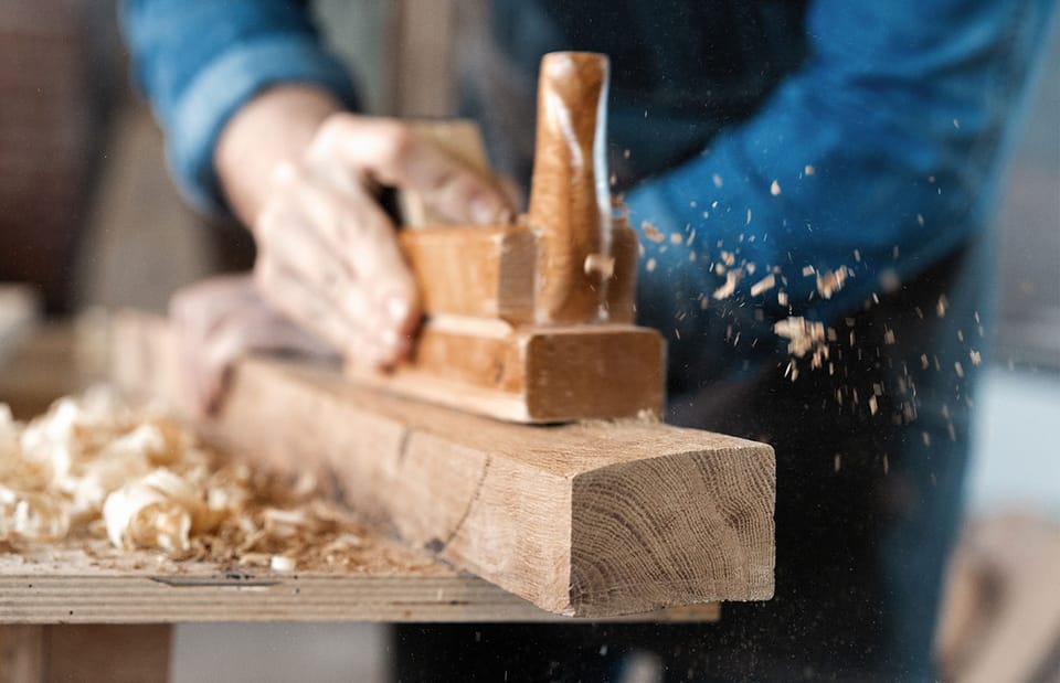 Ein Schreiner arbeitet mit dem Hobel an einem Holzstück