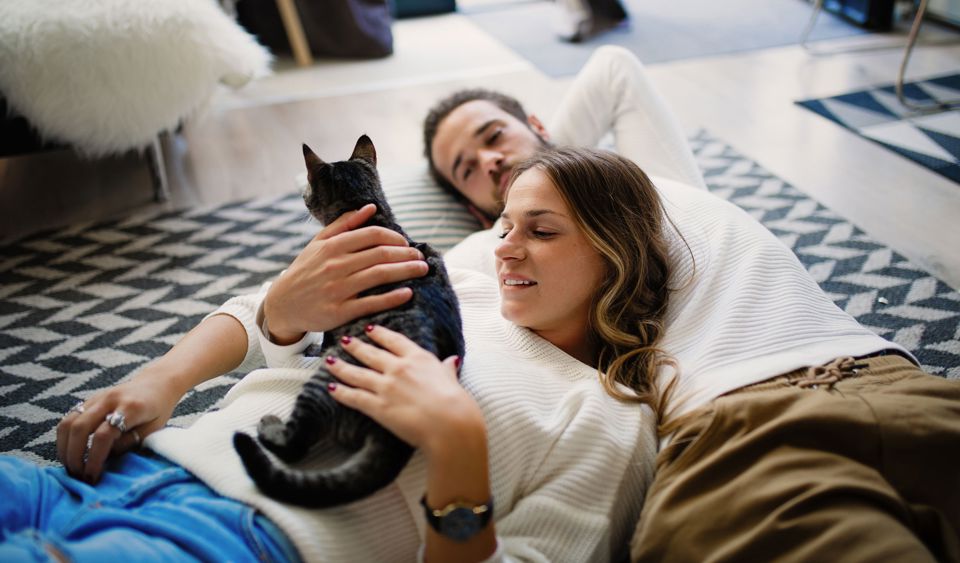 Ein junges Paar mit Katze liegt entspannt auf dem Boden ihrer neuen Eigentumswohnung