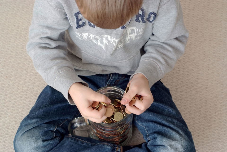 Ein Junge sitzt vor einem mit Münzen gefüllten Glaskrug und fügt weitere Münzen hinzu